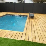 Aménagement extérieur à Thoiry avec pose de terrasse en bois autour de la piscine, pose de clôture en panneaux composite et pose de gazon synthétique