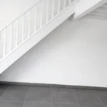 Rénovation d’un appartement pour investissement locatif avec pose de carrelage gris anthracite et peinture complète des murs, escalier et poutres à Saint-Genis-Pouilly